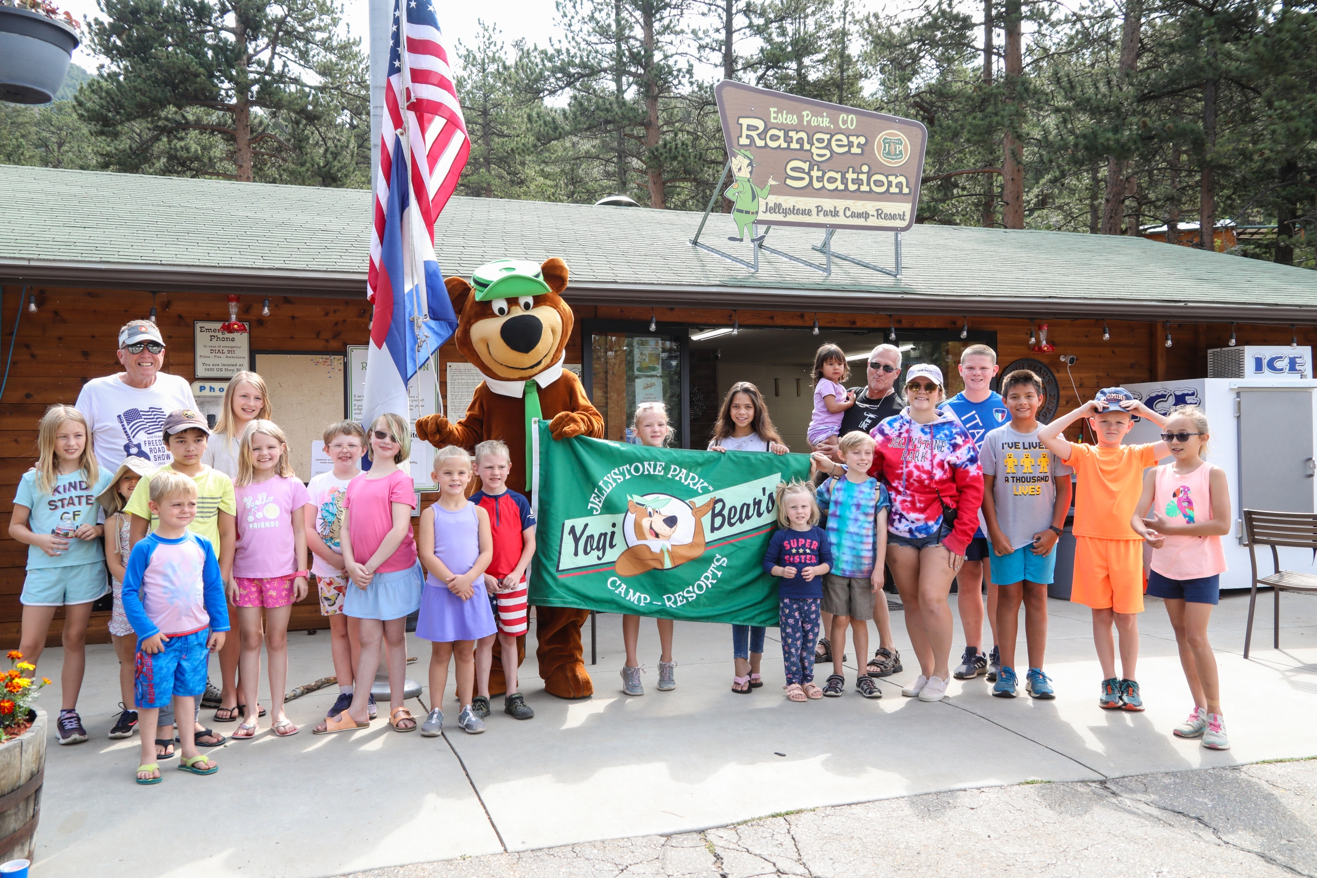 Yogi Bear holding a Camp Jellystone flag posing with a group of campers